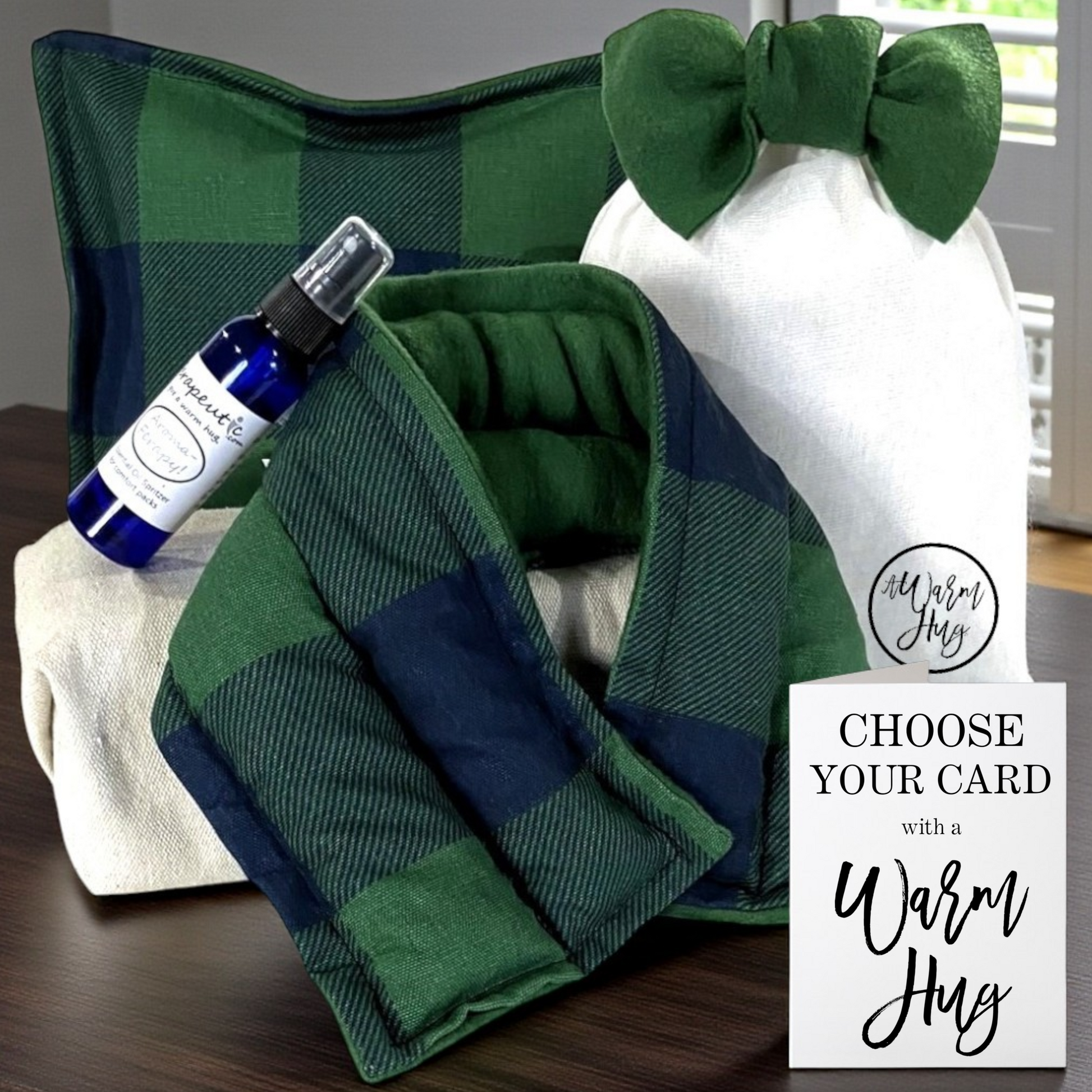 Green and navy checkered microwave heating pad with a bottle of essential oil and gift bag with green bow and a card on a wooden surface.