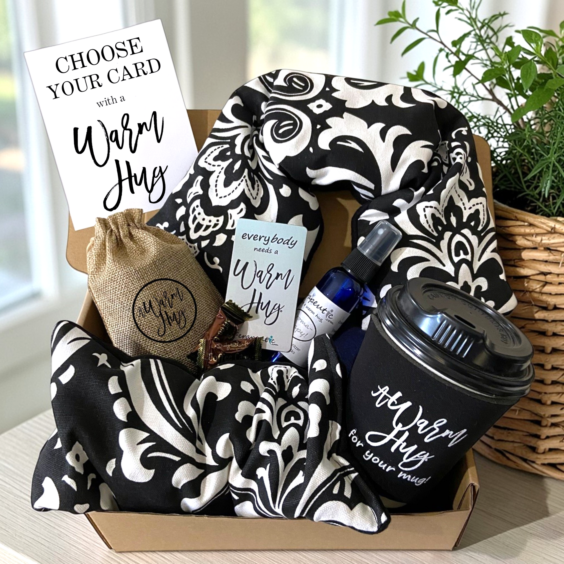 Warm Hug Gift set with black and white patterned microwave neck wrap and eye pillow, coffee cup, burlap bag, magnet, lavender heat pack spray, candies and card in a box.