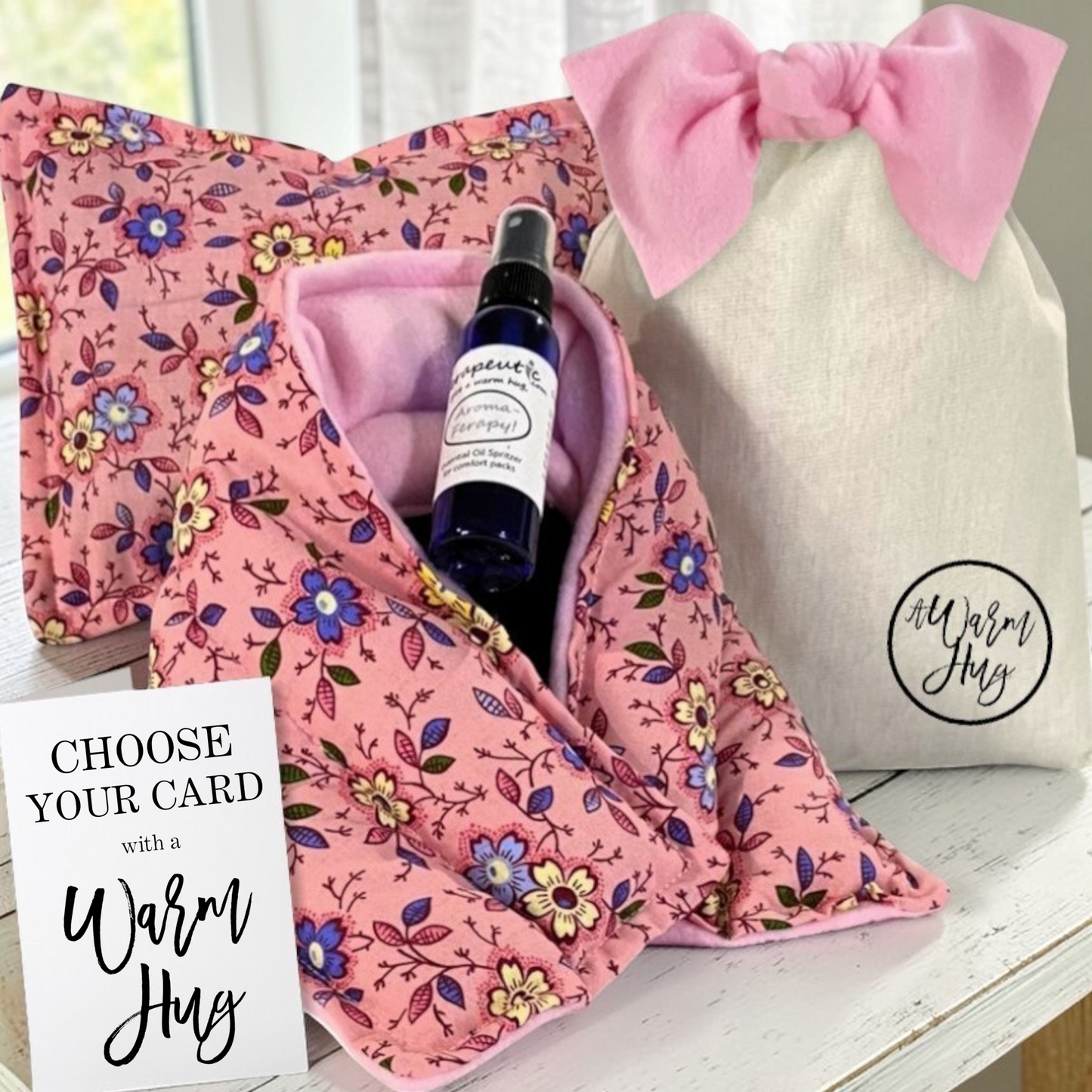 Pink floral fabric with a bottle of aromatherapy spray and a card, next to a white bag with a pink bow.