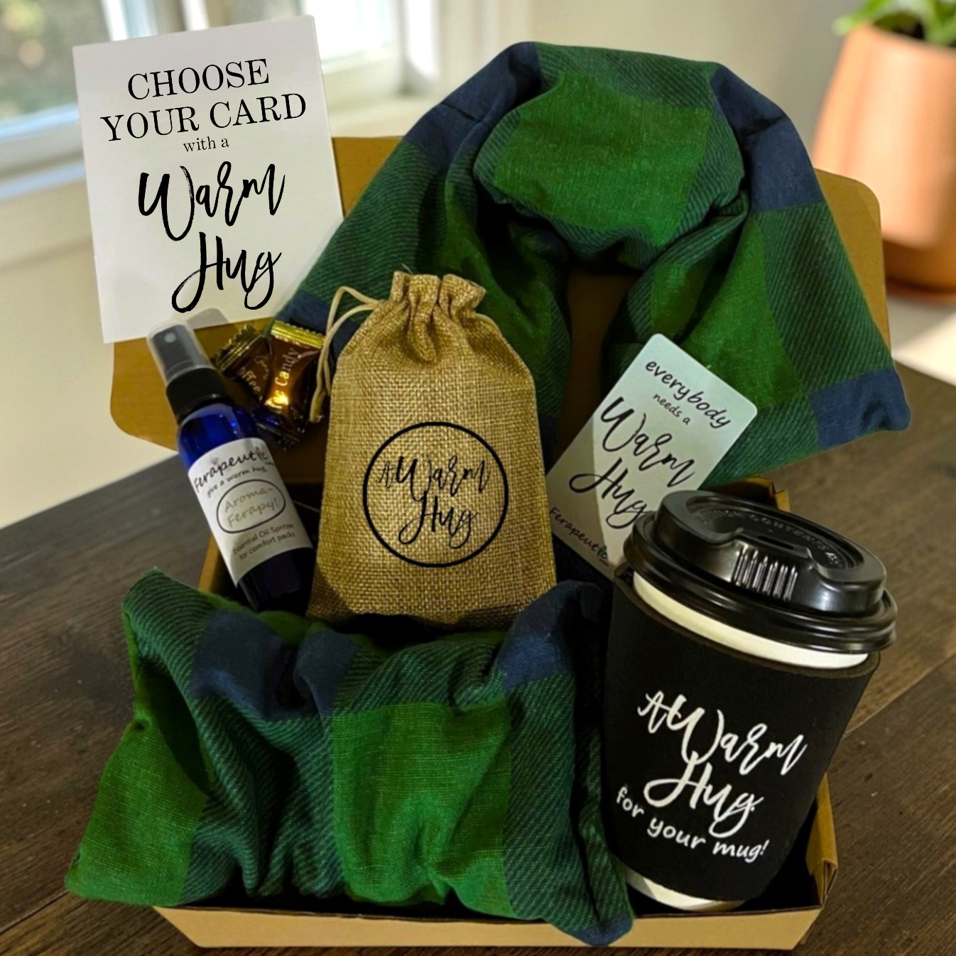 Gift basket with green plaid heating pads, coffee cup, and small bag labeled 'Warm Hug' on a wooden surface.