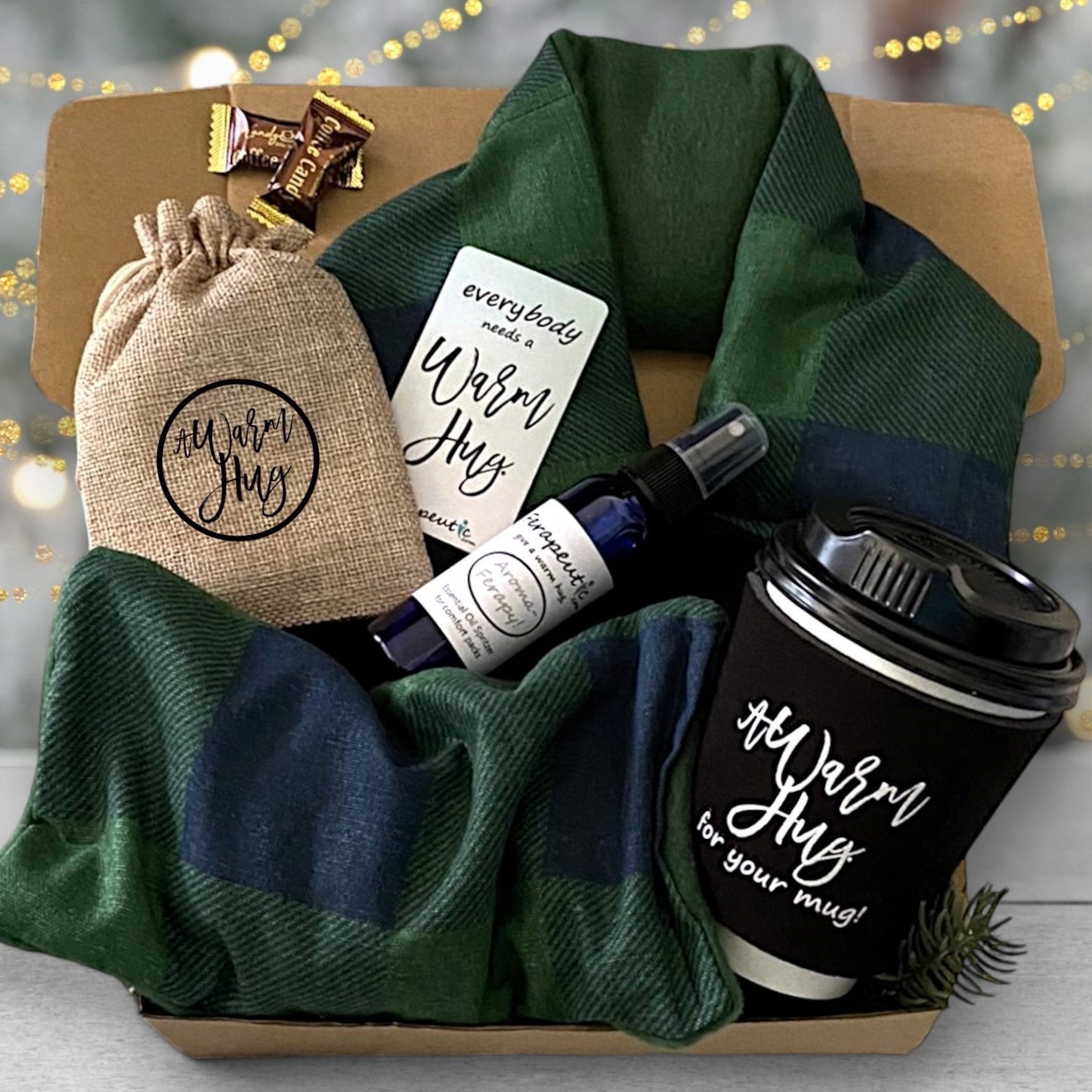 A holiday gift box containing a green heating pad, a burlap bag, an essential oil spray, a black insulated coffee cup sleeve, a fridge magnet, and two candies.