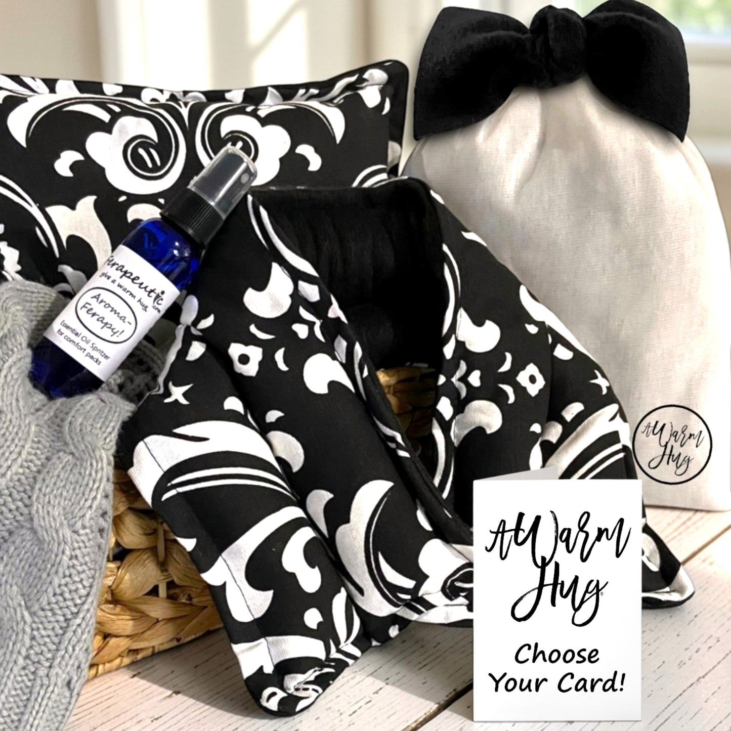Black and white patterned microwavable heat pads with a bottle of essential oil, a bow, and a card on a wooden surface.
