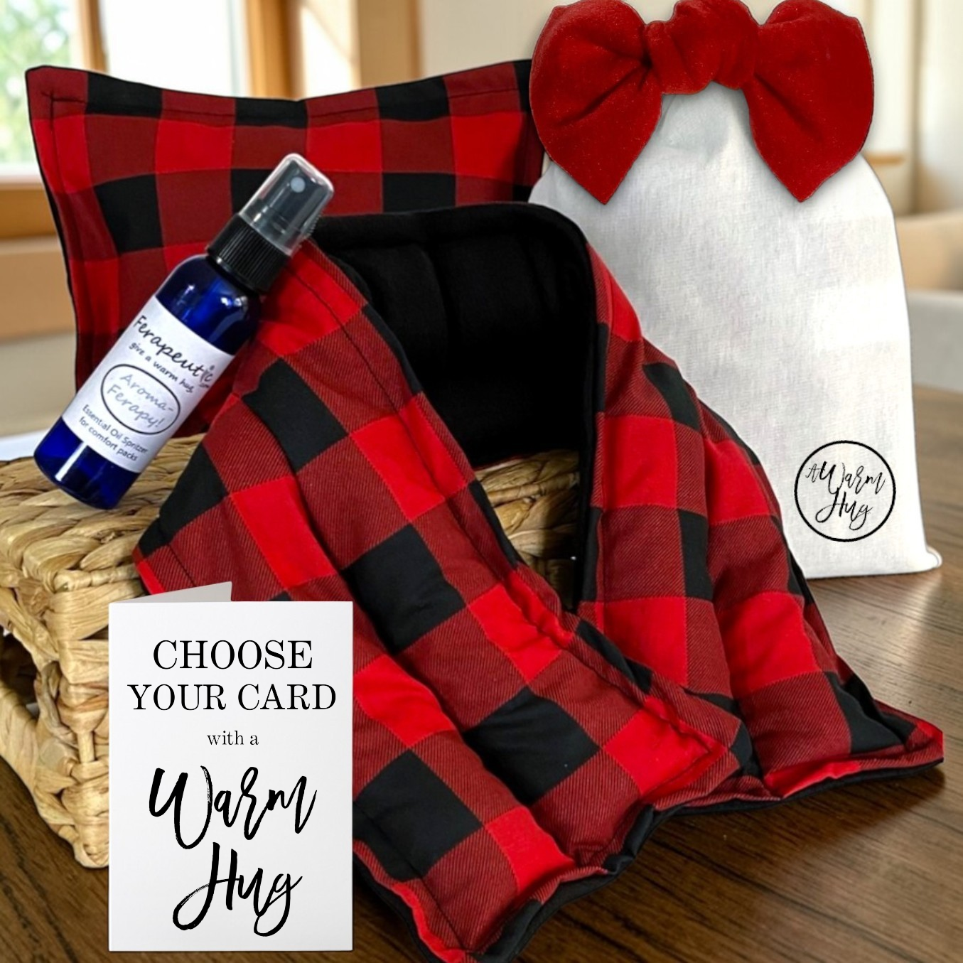 Red and black plaid heat packs with a bottle of essential oil, pillow, warm hug greeting card and gift bag on a wooden surface.